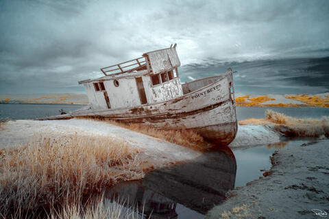 A shipwrecked fishing boat resting atop a sandbar is reflected in a tidal pool.
