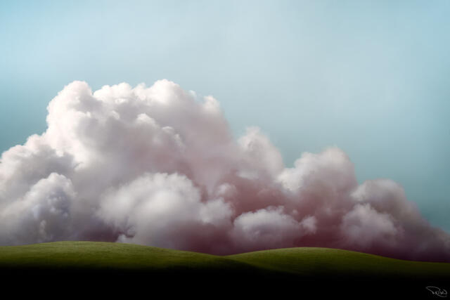A false-color infrared image shows a looming bank of pastel-colored storm clouds casting shadows over a spring green hill.