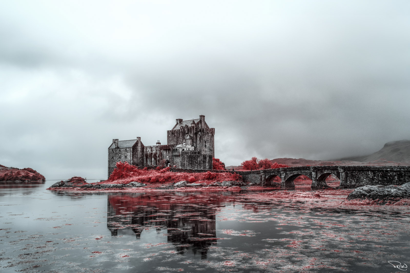 A false-color infrared image of Eilean Donan Castle on a moody, foggy day shows unusual red foliage reflected in the loch.