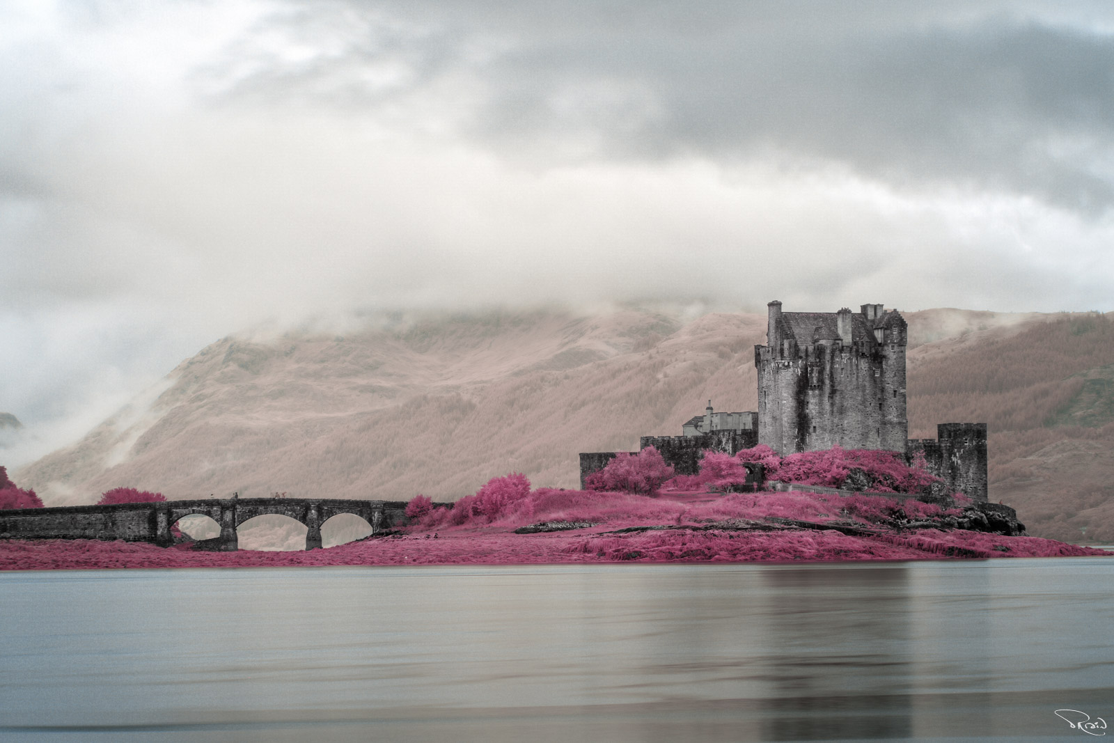 A 13-century stone castle sits on an island surrounded by deep pink heather. Fog is creeping down the hills in the background.